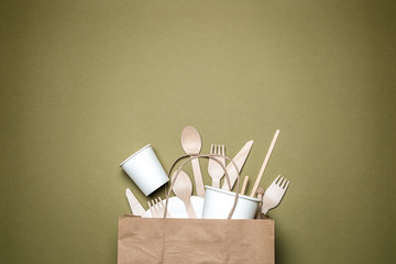 The concept of eco-friendly disposable tableware made of paper and wood on a green background. Top...