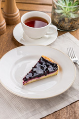 piece of blueberry cheesecake with cup of tea on wooden table