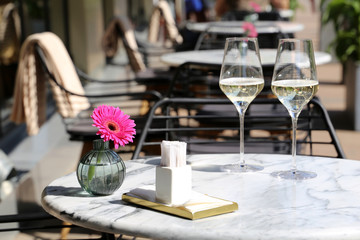 Table set in a street restaurant, romantic meal, elegant setting for celebration and date. Two glasses of champagne, napkins and flower on a table in cafe