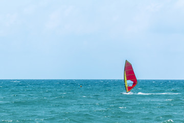 Summer Windsurfing. Male sportsman standing on a sailboard and gliding along the sea waves on a...