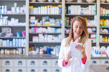 Portrait of pharmacist holding digital tablet in pharmacy. Pharmacist working with a tablet-pc in the pharmacy holding it in her hand while reading information