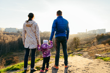 Obraz na płótnie Canvas young family of three standing on the top of the hill with beautiful view of sunset