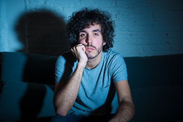 Portrait of bored sleepless young man sitting on the couch watching TV at night