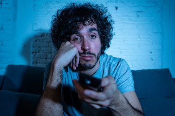 Portrait of bored sleepless young man sitting on the couch watching TV at night
