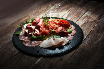 Food tray with delicious salami, pieces of sliced ham, sausages,salad and vegetable. Meat platter with selection