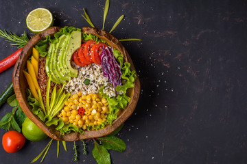 Fototapeta na wymiar Buddha bowl with chickpea, avocado, wild rice, quinoa seeds, bell pepper, tomatoes, greens, cabbage, lettuce on shabby dark stone table. Vegetarian super food. Top view with copy space.