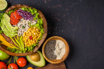 Buddha bowl with chickpea, avocado, wild rice, quinoa seeds, bell pepper, tomatoes, greens, cabbage, lettuce on shabby dark stone table and wooden bowl with chia and sesame seeds. Top view.