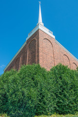 Beautiful stone church with white spire - clear vivid blue skies with lush green bushes in front - wide angle - green, brown, white, and blue