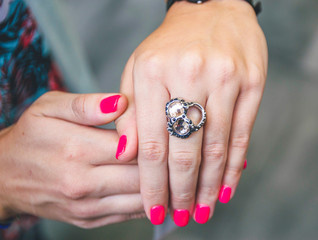 Big fashion ring on the hand with pink manicure. Neon color shade of nail polish. Close up picture of beauty. Accessories for women.