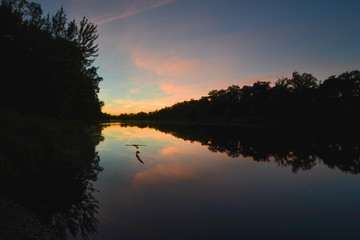 Sunset on the St. Croix River between Minnesota and Wisconsin - darkened trees reflected on the calm waters - blue, orange, pink colors in the clouds of the sky