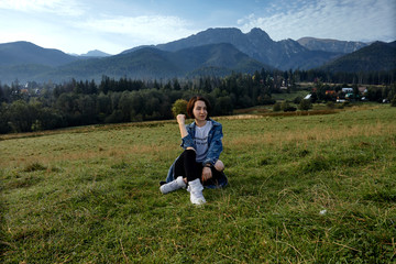 Fototapeta na wymiar Girl sitting on grass. Mountains as a background