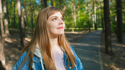 Naklejka premium Calm beautiful smiling young woman enjoying fresh air , relaxing , feeling alive, breathing, dreaming. Copy space, green park nature background. Side view portrait