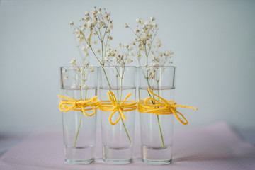 floral decoration: three small glass vases with white flowers; gypsophila on a blue background; yellow canvas bows