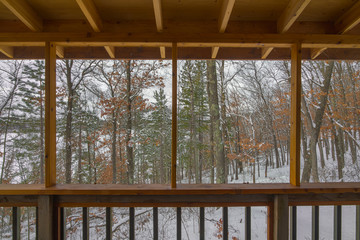 Beautiful snowy winter view of a Northwoods mixed forest (deciduous and coniferous) through a screened-in porch on a rustic cabin off a remote lake in Northern Wisconsin