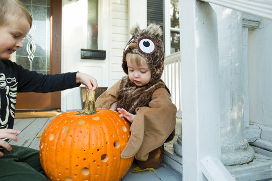 Two children examine jack o lantern on front porch during Halloween