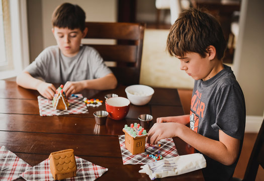 Two boys decorating gingerbread houses together at the table.