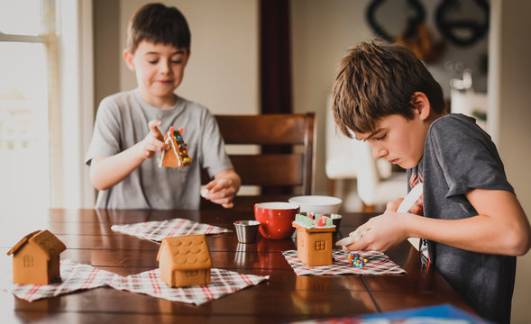 Two boys decorating gingerbread houses together at the table.