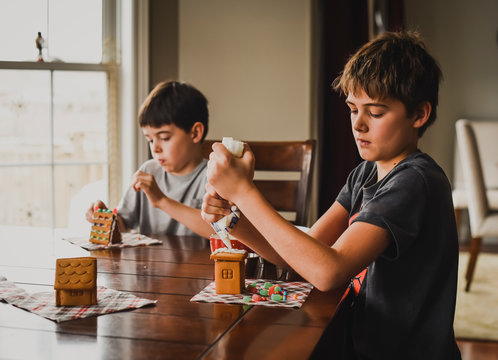 Siblings decorating gingerbread houses on table
