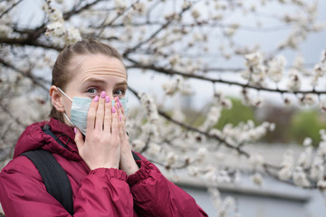 Young woman in protective medical face mask. Blooming tree on background. Spring allergy.