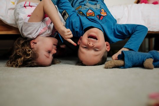 young boy and girl siblings laughing together upside-down on bed