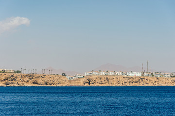 hotels and houses in the distance stand over a cliff above the blue sea.