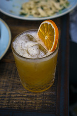 old-fashioned whiskey cocktail with an orange with food in the background