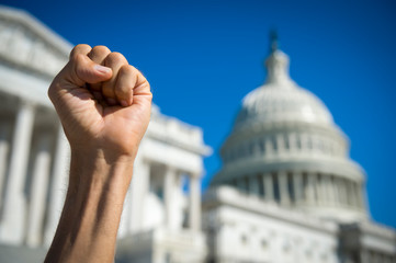 Angry fist of a protestor in the air under bright blue sky on a sunny day at Capitol Hill in...
