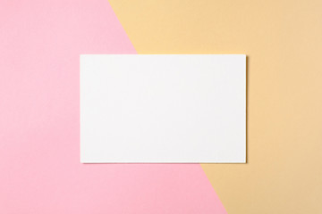 Obraz na płótnie Canvas Blank white paper card on two color pastel pink and yellow background. Flat lay, top view, overhead. Creative layout, greeting card with free space for text, banner template, mockup for beauty blog.