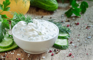 Ranch whte sauce in white bowl with cucumber, herbs and spices on old wooden table, selective focus - obrazy, fototapety, plakaty