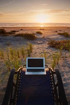 Laptop on deck chair overlooking sunset on beach