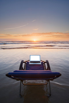 Laptop On Deck Chair Overlooking Sunset On Beach