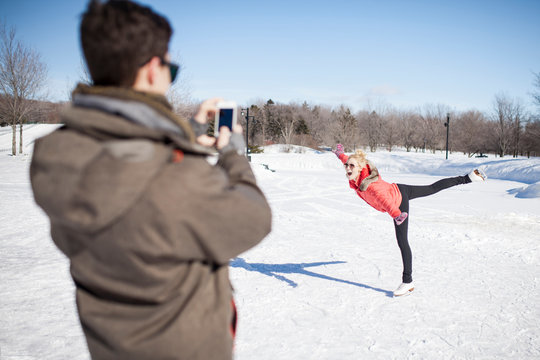 Caucasian man taking picture of girlfriend ice skating on frozen lake