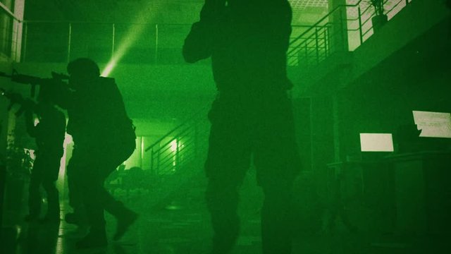 Masked Squad of Armed SWAT Police Officers Slowly Move in a Hall of a Dark Seized Office Building with Desks and Computers. Soldiers with Rifles Cover Surroundings. Green Night Vision Effect.