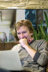 a middle-aged man watches the news on a laptop and is horrified