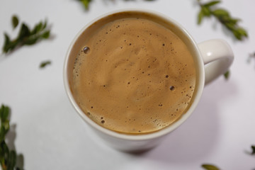 White mug with a hot drink on a background of dry green petals on a white background. Composition of coffee mug with milk and dry green petals on a paper background. Healthy drink in a white mug