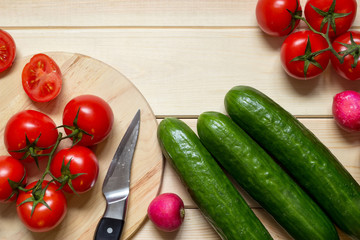 Kitchen table with fresh vegetables, knife and sliced tomato.