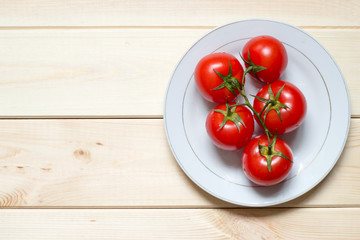 Ripened tomatoes on white plate on light wooden table with copy space