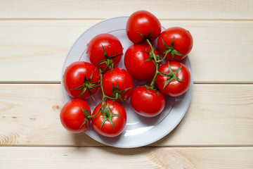 Washed red ripened cherry tomatoes on white plate on light wooden table