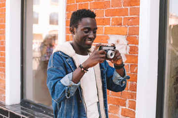 Portrait happy smiling young african man with vintage film camera taking picture walking on city street over brick wall background