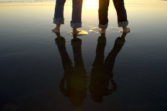 Reflection of legs in water at beach