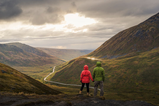 Asian hikers holding hands admiring scenic view of valley