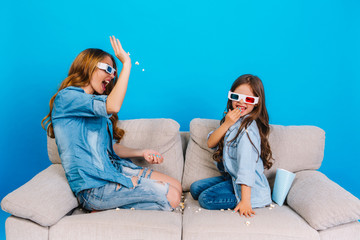 Happy moments of pretty young mother having fun with daughter on couch isolated on blue background....