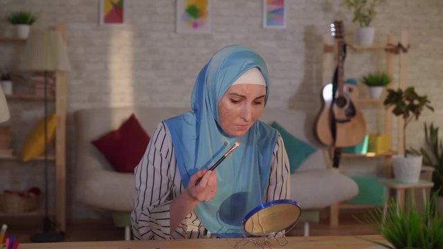 Young arab woman in hijab with burn scar on her face doing makeup and crying