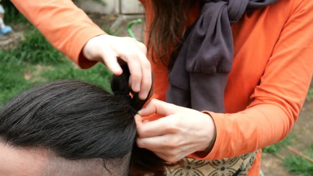Woman hairdresser braids young man long hair in a braid. Outdoors. Close-up.