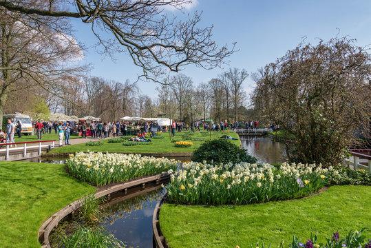 Outdoor sunny view of visitors and tourists enjoy open air market with natural atmosphere of the park and tulip garden around pond or canal at Keukenhof garden.