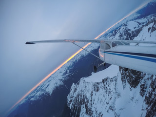 Obraz premium Aerial view of a small airplane flying over the Canadian Mountain Landscape during a gloomy cloudy sunset. Taken near Squamish, North of Vancouver, British Columbia, Canada.