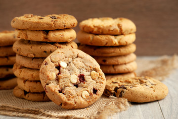 A pile of oatmeal cookies. A lot of oatmeal cookies on wooden background. Baking with nuts, chocolate and jam on burlap. Dry breakfast.