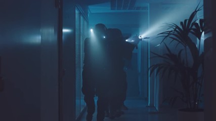 Masked Team of Armed SWAT Police Officers Slowly Move in a Hall of a Dark Seized Office Building with Desks and Computers. Soldiers with Rifles and Flashlights Surveil and Cover Surroundings.