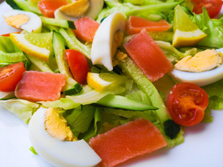 Closeup view of plate full of fresh green salad with mint leaves, yellow corn, tomato, tuna fish served with juicy lemon sauce. Person eats healthy food.