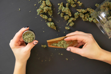 Pot use concept. Top view of marijuana blunt with grinder. Woman preparing and rolling marijuana...